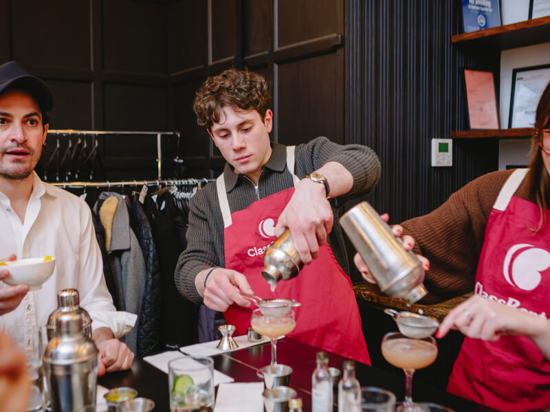 Man in red ClassBento apron pouring a cocktail into a glass